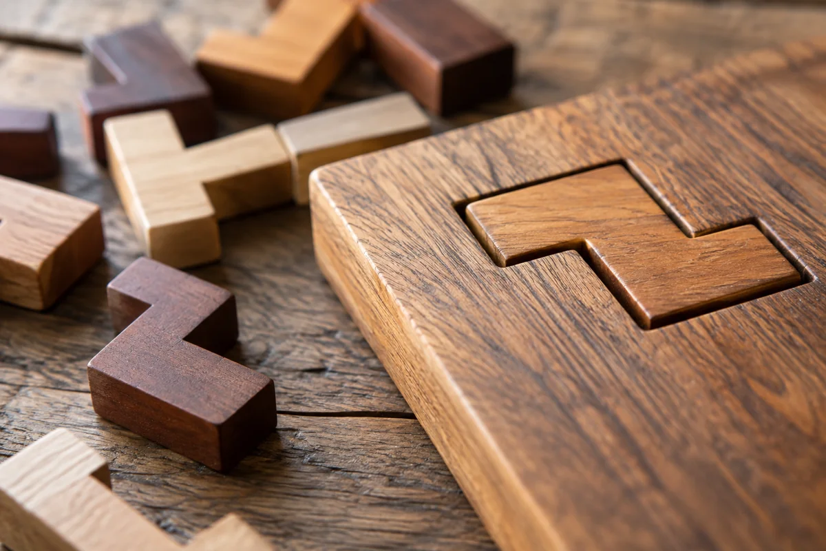 Set of mismatched wooden puzzle blocks beside a neat custom-cut block that fits a carved slot