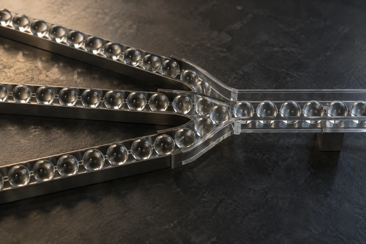 Separate rows of glass marbles converging into a single clear channel on a dark surface