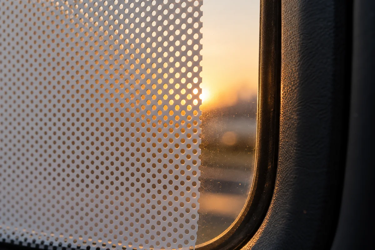 Macro view of perforated white vinyl film edge on clear glass with fine regular holes and soft evening light behind