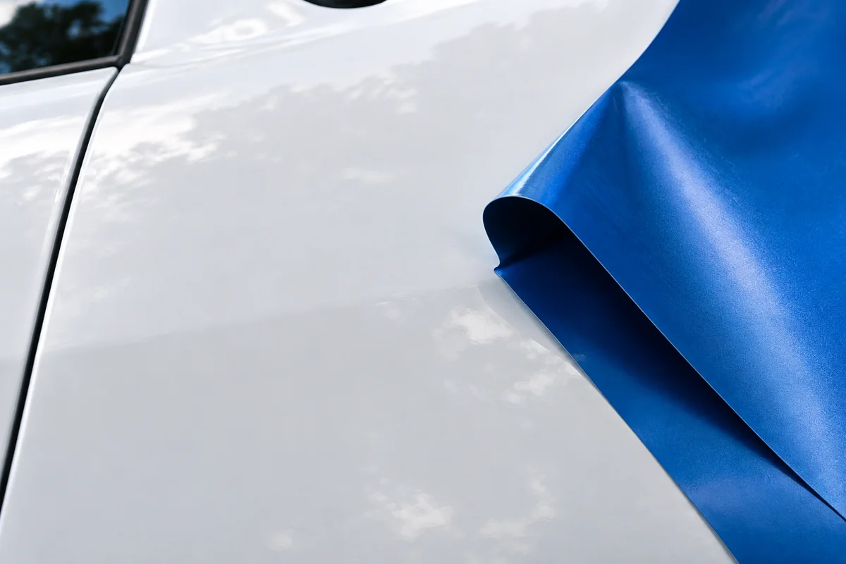 Close-up of a clean white vehicle panel beside a curled blue vinyl sample